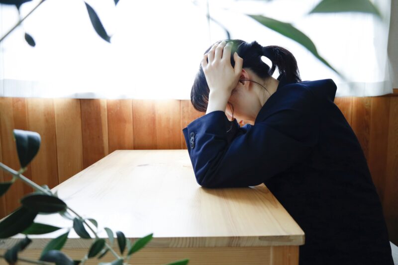 頭を抱えて座っているジャケット姿の女性