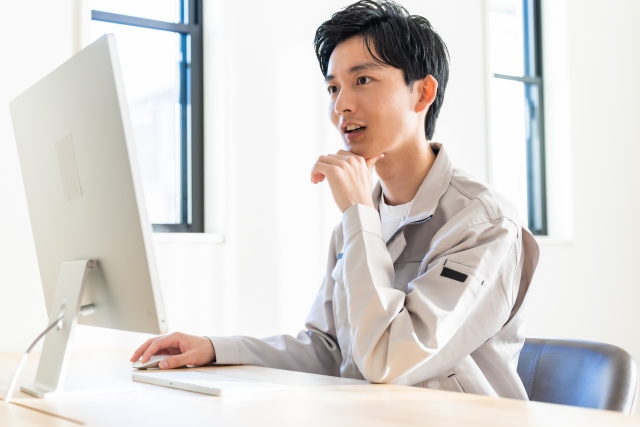 パソコン作業をする作業着を着た男性