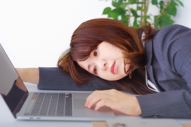 職場のデスクで辛そうな表情をしている女