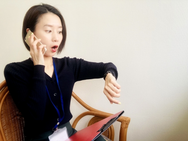 電話をしながら腕時計を見て驚く社会人